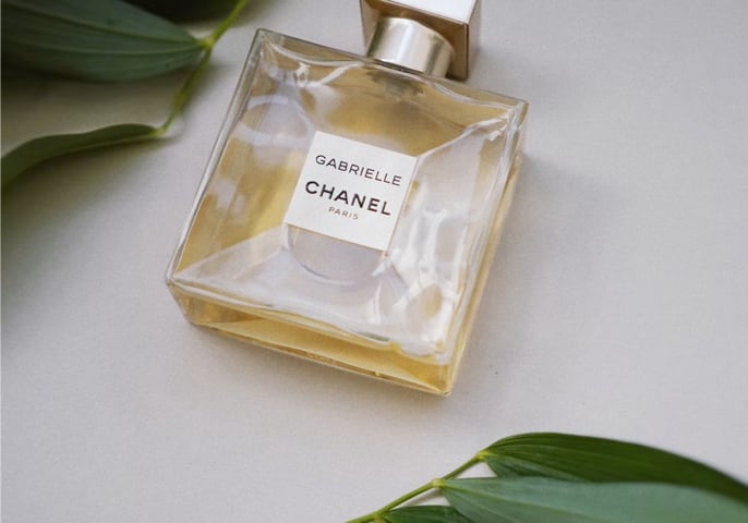 A Bottle of Gabrielle Essence Eau De Parfum on floor 
          with leaves on the sides